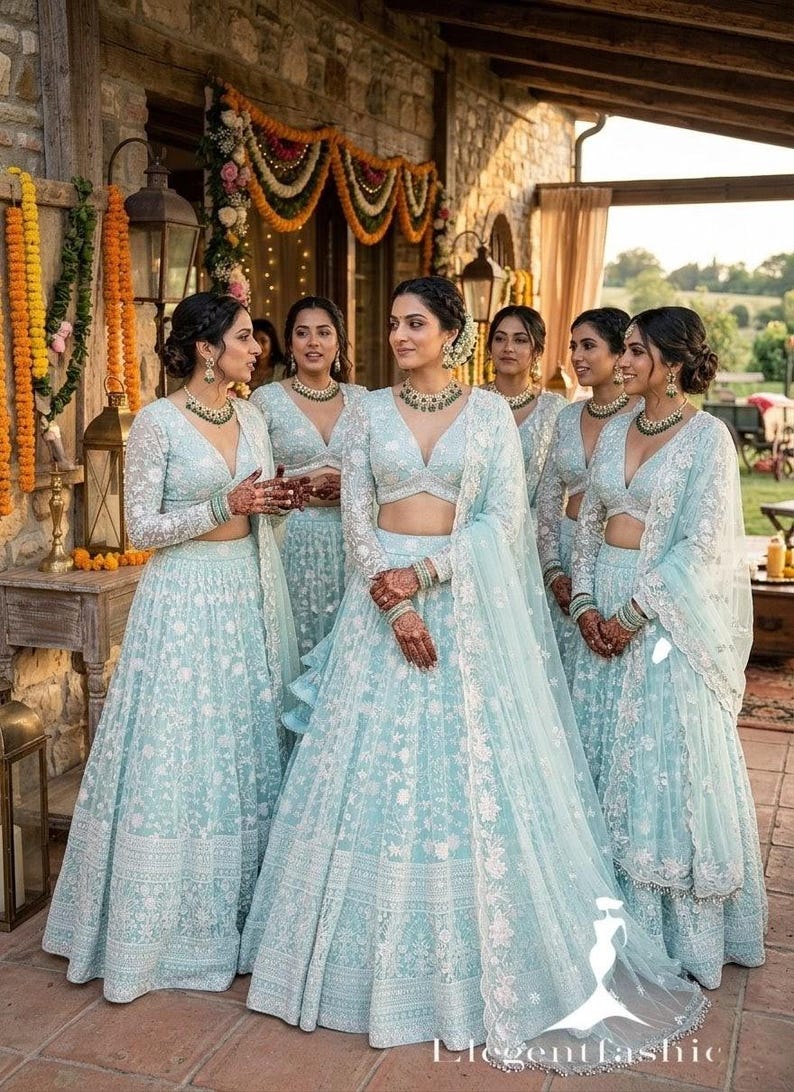 May include: A group of women in matching light blue formal dresses with intricate white floral embroidery. The dresses feature long sleeves, V-necklines, and flowing skirts. They are adorned with matching jewelry and henna designs.