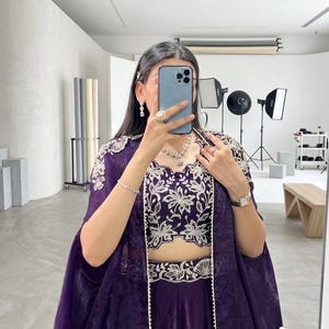 Puede incluir: Un conjunto formal morado con un top corto y un conjunto de falda con intrincados bordados florales blancos. Una chaqueta larga a juego completa el atuendo. El atuendo est&aacute; adornado con joyas.