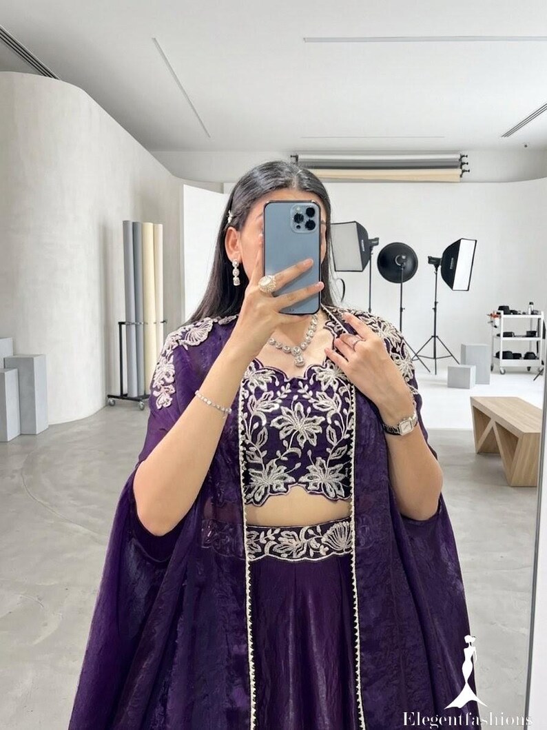 Puede incluir: Un conjunto formal morado con un top corto y un conjunto de falda con intrincados bordados florales blancos. Una chaqueta larga a juego completa el atuendo. El atuendo est&aacute; adornado con joyas.