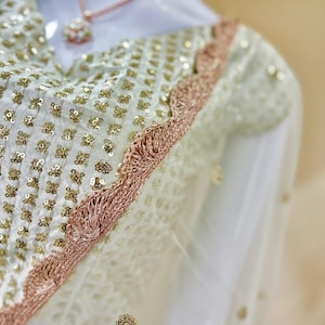 Op de afbeelding: Een witte blouse met een ruitpatroon van kleine gouden lovertjes, geaccentueerd door een geschulpte ros&eacute;gouden metalen rand langs de halslijn en schouder. Een fijne ros&eacute;gouden ketting rust op de stof en de tekst Elegantfashions is zichtbaar.