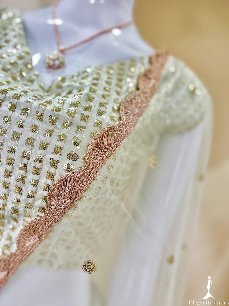 Op de afbeelding: Een witte blouse met een ruitpatroon van kleine gouden lovertjes, geaccentueerd door een geschulpte ros&eacute;gouden metalen rand langs de halslijn en schouder. Een fijne ros&eacute;gouden ketting rust op de stof en de tekst Elegantfashions is zichtbaar.