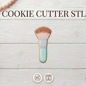 May include: A cookie cutter in the shape of a makeup brush, featuring a light brown brush head, a grey handle section, and a light blue handle. The text "COOKIE CUTTER STL" is at the top. The image is on a white wooden background.