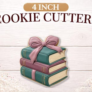 May include: A stack of three cookie cutters shaped like books, topped with a bow. The cookie cutters are teal and mauve with gold accents. The text "4 INCH COOKIE CUTTERS" is above the cookies.