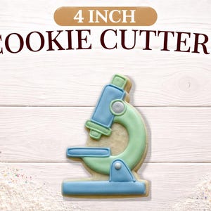 May include: A 4-inch cookie cutter shaped like a microscope, with blue and green icing details. The words "4 INCH COOKIE CUTTERS" are displayed above the cookie cutter on a white wooden background.
