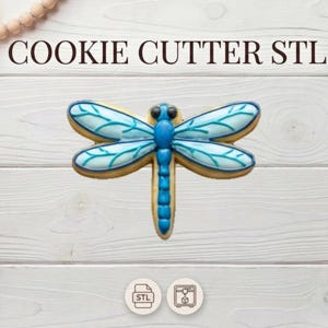 May include: A dragonfly-shaped cookie cutter with blue and white details, set against a white wooden background. The text "COOKIE CUTTER STL" is displayed above the cookie cutter. Decorative elements include a string of wooden beads and a bouquet of dried flowers.