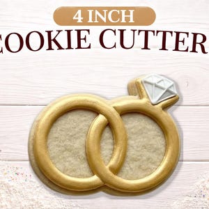 May include: A 4-inch cookie cutter in the shape of two interlocking wedding rings, one with a diamond-shaped gem. The rings are gold-colored, and the gem is white. The text "4 INCH COOKIE CUTTERS" is at the top.