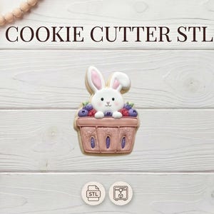 May include: A bunny-shaped cookie cutter with a basket of berries. The cookie cutter is pink and white, with the text "COOKIE CUTTER STL" at the top. The image is on a white wooden background.
