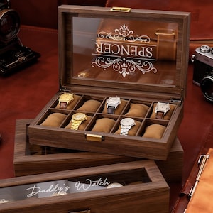 May include: A wooden watch display case with a glass top, holding several wristwatches. The case is open, revealing the watches on brown cushions. The top of the case is engraved with the name "Spencer". A smaller case below reads "Daddy's Watch".