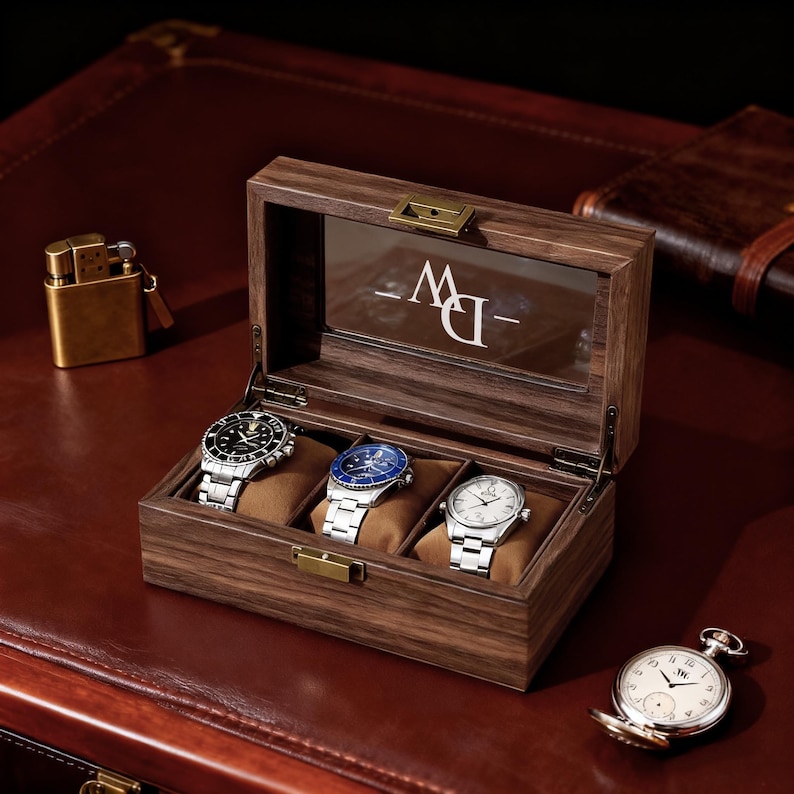May include: A wooden watch box with three watches inside, each resting on a brown cushion. The box has a glass top and a metal clasp. A gold lighter and a pocket watch are also visible.