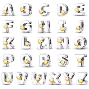 May include: A selection of silver alphabet charms, each with a gold heart detail. The letters A to Z are shown, displaying diverse designs. These charms are likely for bracelets or necklaces.