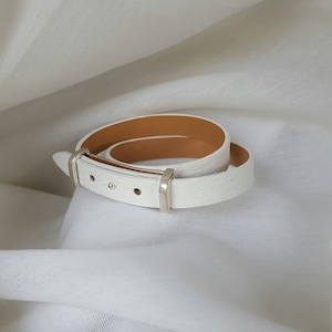 May include: White leather bracelet with a silver buckle. The bracelet is double-layered and has a brown leather lining.