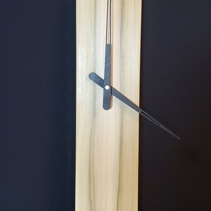 May include: A wooden clock with black hands on a light wood background. The clock is rectangular and has a simple design.