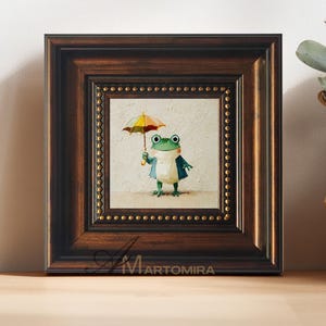 Pode incluir: Uma pintura quadrada emoldurada apresentando um sapo verde segurando um guarda-chuva multicolorido. O sapo tem uma barriga clara e veste um casaco azul. A moldura é castanho-escura com uma borda interna dourada. O texto Martomira é visível.