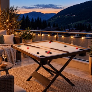 May include: A square wooden carrom board game table with a light-colored playing surface, dark wooden edges, and black metal cross-legs. The board features four corner pockets, a long wooden striker, and several red and black circular game pieces.