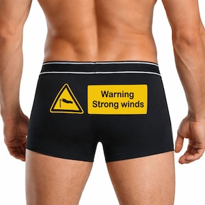 May include: Black boxer briefs with a white waistband and the text "Warning Strong winds" on the back. The briefs feature a yellow warning sign with a windsock graphic.