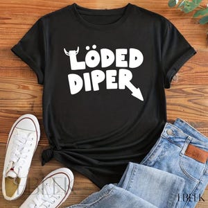 May include: Black t-shirt with the text "LÖDED DIPER" in white, featuring a bull's head and an arrow. The shirt is paired with blue jeans and white sneakers, creating a casual, everyday look.