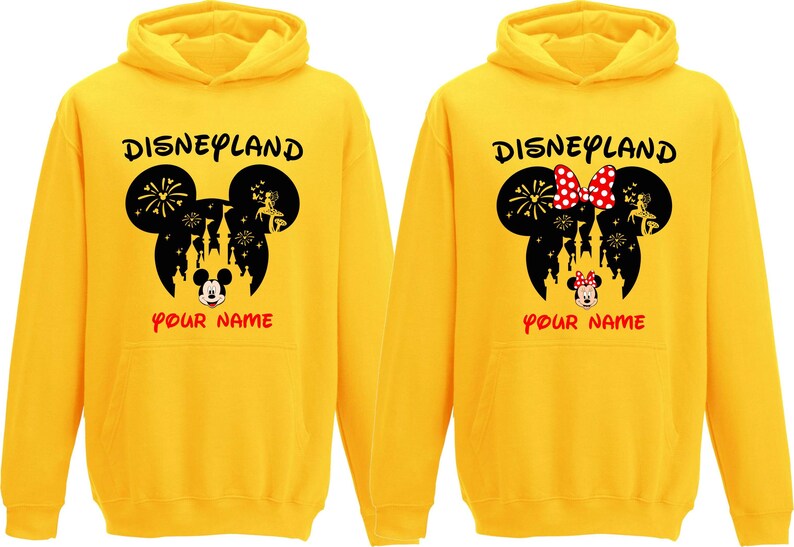 以下が含まれることがあります： 「Disneyland」の文字と黒いミッキーマウスの頭のシルエットがプリントされた2つの黄色のパーカー。1つはミッキーマウスのデザイン、もう1つは赤い水玉模様のリボンが付いたミニーマウスのデザインです。「YOUR NAME」の文字が下にあります。