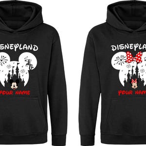 以下が含まれることがあります： 黒いパーカー。デザインは、花火、お城、赤い「Your Name」の文字と「Disneyland」の文字が上に書かれた白いミッキーマウスの頭が特徴です。1つは赤いリボンが付いています。