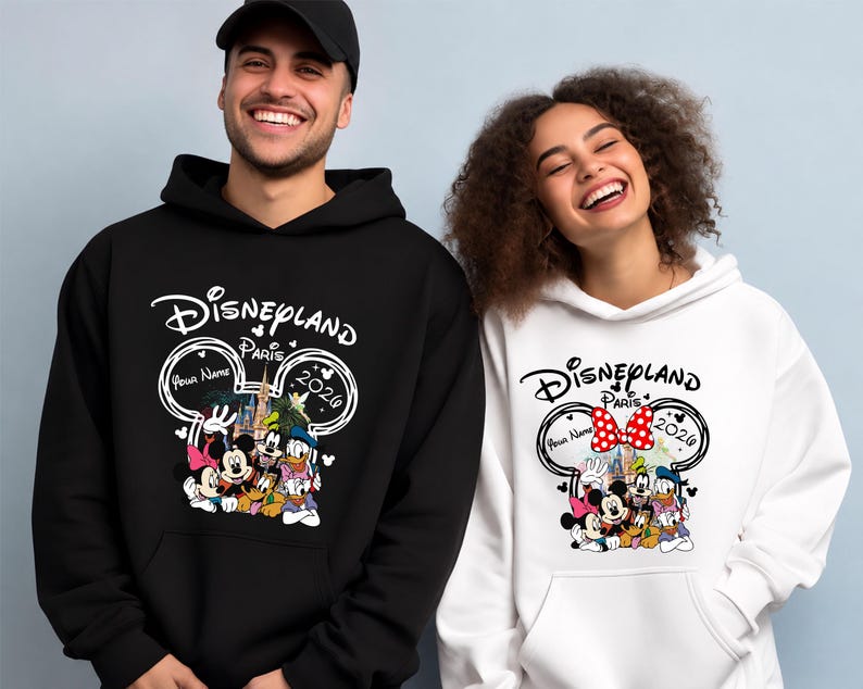 Puede incluir: Sudaderas con capucha negras y blancas de Disneyland Par&iacute;s 2026. El dise&ntilde;o presenta a Mickey y Minnie Mouse, el Pato Donald y Goofy. El texto "Disneyland Par&iacute;s" est&aacute; arqueado sobre los personajes. El dise&ntilde;o incluye el texto "Your Name" y el a&ntilde;o "2026".