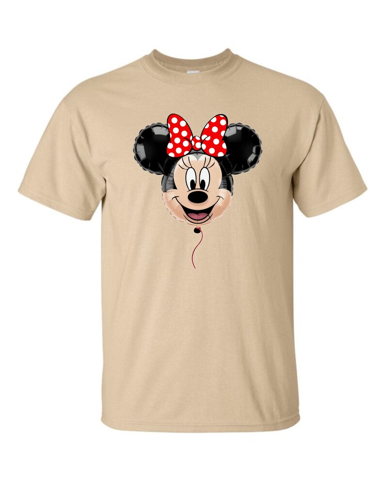 Pu&ograve; includere: T-shirt color cachi con un design a palloncino di Minnie Mouse. Il palloncino ha orecchie nere, una faccia sorridente e un fiocco rosso a pois bianchi. Un filo rosso pende sotto.