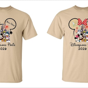 May include: Two tan t-shirts with a Disneyland Paris 2026 design. The design features Mickey Mouse ears, Disney characters, and the text "Your Name". One shirt has a red bow, the other does not.