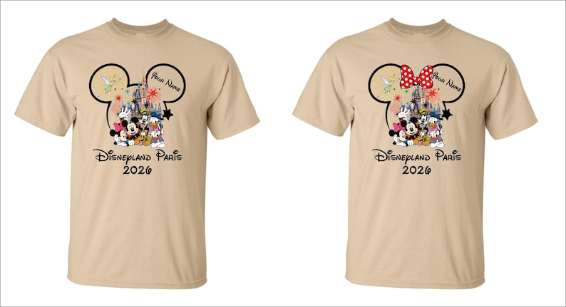 May include: Two tan t-shirts with a Disneyland Paris 2026 design. The design features Mickey Mouse ears, Disney characters, and the text "Your Name". One shirt has a red bow, the other does not.