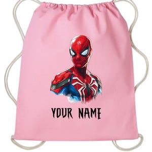 May include: A pink drawstring backpack featuring a detailed illustration of Spider-Man. The superhero is depicted in his classic red and blue suit. The text "YOUR NAME" is printed in black below the image.