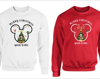 May include: Two sweatshirts, one white and one red, feature a Mickey Mouse head design with a Christmas tree and the text "MERRY CHRISTMAS" and "YOUR NAME". The red sweatshirt has a Minnie Mouse bow.