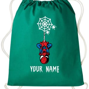 Puede incluir: Mochila con cord&oacute;n de color verde azulado con un dise&ntilde;o de Spider-Man. El dise&ntilde;o incluye una telara&ntilde;a blanca, ara&ntilde;as y Spider-Man boca abajo. El texto "YOUR NAME" est&aacute; impreso en blanco. Cuerdas blancas.