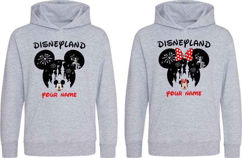 以下が含まれることがあります： 「Disneyland」の文字と黒いミッキーマウスの頭のデザインが施された2つのグレーのパーカー。1つのパーカーには、白のドットが付いた赤いリボンが付いています。「YOUR NAME」の文字が赤色で下に印刷されています。