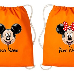 Może przedstawiać: Dwie pomarańczowe torby ze sznurkiem ze stylizowanymi twarzami Myszki Miki i Myszki Minnie. Miki ma uśmiechniętą twarz, a Minnie czerwoną kokardę w kropki. Każda torba ma napis "Your Name" czarnym pismem.