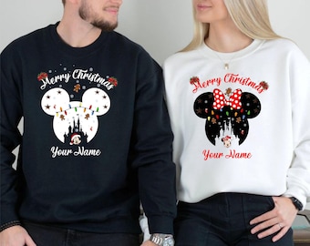 May include: Black and white sweatshirts with a Christmas design. The black sweatshirt has a white Mickey Mouse head with a castle, lights, and the text "Merry Christmas" and "Your Name". The white sweatshirt has a Minnie Mouse head with a red bow and the same text.