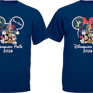 May include: Two navy blue t-shirts featuring a Disney design. The design includes Mickey Mouse ears, a castle, and various Disney characters. The text "Disneyland Paris 2026" is printed below the characters. One shirt has a red bow.