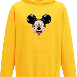 May include: A yellow hooded sweatshirt featuring a Mickey Mouse balloon graphic. The graphic shows Mickey's face with black ears and a smiling expression. The sweatshirt has a front pocket and a drawstring hood.