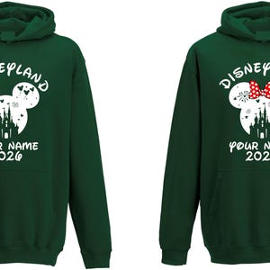 May include: Two dark green hoodies with white text and graphics. The hoodies feature a Mickey Mouse head design with a castle silhouette and the text "Disneyland", "Your Name", and "2026". One hoodie has a red bow.