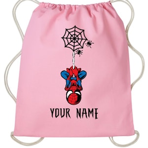 Puede incluir: Mochila con cord&oacute;n rosa con un dise&ntilde;o de Spider-Man. El dise&ntilde;o incluye una telara&ntilde;a negra, ara&ntilde;as y Spider-Man colgado boca abajo. El texto "YOUR NAME" est&aacute; impreso en negro.