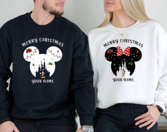 May include: Black and white sweatshirts with a Christmas-themed Mickey Mouse design. The design includes a castle, holiday lights, and the text "MERRY CHRISTMAS" and "YOUR NAME". One sweatshirt is black, the other is white.