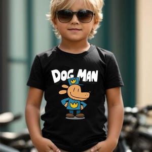 May include: A black t-shirt featuring the text "DOG MAN" above a cartoon dog character in a police uniform. The child is wearing sunglasses and khaki pants. The background is a blurred outdoor scene.