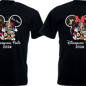 May include: Black t-shirts featuring a Mickey Mouse head design with Disneyland Paris 2026 text. One shirt has a red bow, the other does not. The design includes Disney characters, fireworks, and the text "Your Name".