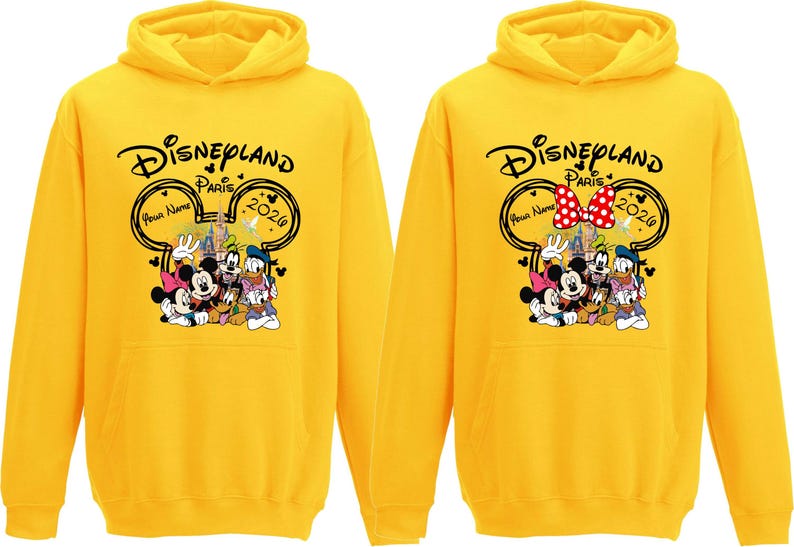 Puede incluir: Dos sudaderas con capucha amarillas con el logotipo de Disneyland Paris, con Mickey Mouse, Minnie Mouse, el Pato Donald, Goofy y Pluto. Las sudaderas tienen el texto "Disneyland Paris 2026" y un espacio para un nombre.