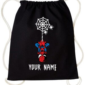 Puede incluir: Mochila con cord&oacute;n negra con un dise&ntilde;o de Spider-Man. Muestra una telara&ntilde;a blanca, dos ara&ntilde;as y Spider-Man colgado boca abajo. El texto "YOUR NAME" est&aacute; impreso en blanco.