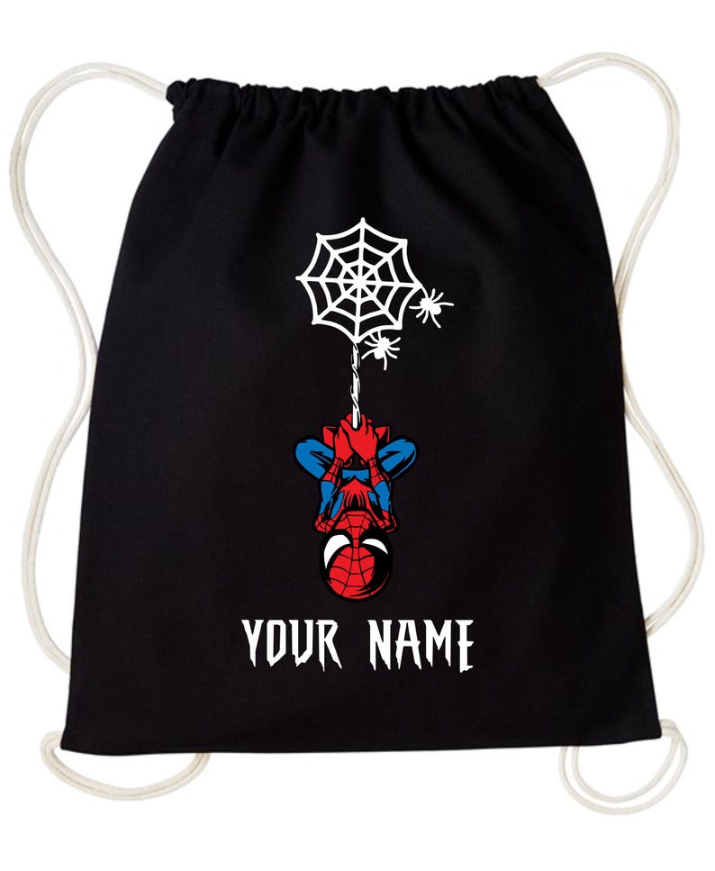 Puede incluir: Mochila con cord&oacute;n negra con un dise&ntilde;o de Spider-Man. Muestra una telara&ntilde;a blanca, dos ara&ntilde;as y Spider-Man colgado boca abajo. El texto "YOUR NAME" est&aacute; impreso en blanco.