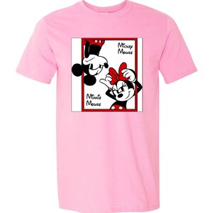 May include: A light pink t-shirt featuring a graphic of Mickey and Minnie Mouse. The graphic is in a red-bordered box with the words "Mickey Mouse" and "Minnie Mouse". Mickey is upside down, and Minnie is right-side up.