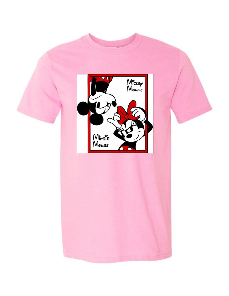 May include: A light pink t-shirt featuring a graphic of Mickey and Minnie Mouse. The graphic is in a red-bordered box with the words "Mickey Mouse" and "Minnie Mouse". Mickey is upside down, and Minnie is right-side up.