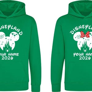 May include: Two green Disneyland hoodies. One features a white Mickey Mouse head with a castle silhouette, fireworks, and the text "YOUR NAME 2026". The other has a red bow.