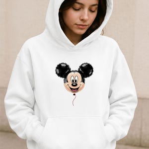May include: White hooded sweatshirt featuring a Mickey Mouse balloon graphic. The graphic shows Mickey's face and ears in black, with a red string. The sweatshirt has a front pocket and a drawstring hood.