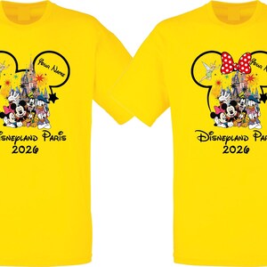May include: Two yellow t-shirts featuring a Disney theme. Each shirt has a Mickey Mouse head outline with a castle, characters, and the text "Disneyland Paris 2026". One shirt has a red and white polka dot bow.
