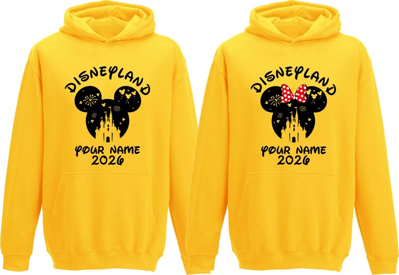 May include: Two yellow Disneyland hoodies. One features a black Mickey Mouse head design with fireworks, a castle, and the text "Disneyland" and "Your Name 2026." The other has a Minnie Mouse head with a red bow.