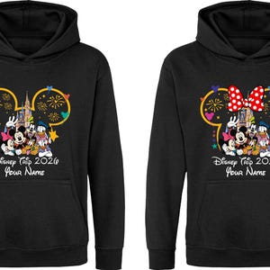 May include: Two black hooded sweatshirts featuring a graphic of Mickey Mouse, Minnie Mouse, Donald Duck, and Goofy in front of a castle with fireworks. The text reads Disney Trip 2026 and Your Name. One hoodie includes a red and white polka dot bow.