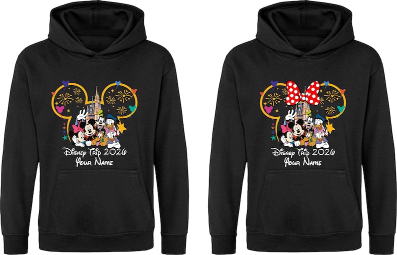 May include: Two black hooded sweatshirts featuring a graphic of Mickey Mouse, Minnie Mouse, Donald Duck, and Goofy in front of a castle with fireworks. The text reads Disney Trip 2026 and Your Name. One hoodie includes a red and white polka dot bow.